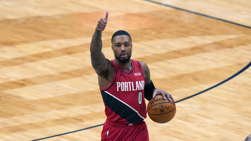 Damian Lillard gives a thumbs up as he dribbles with the other hand during a game.