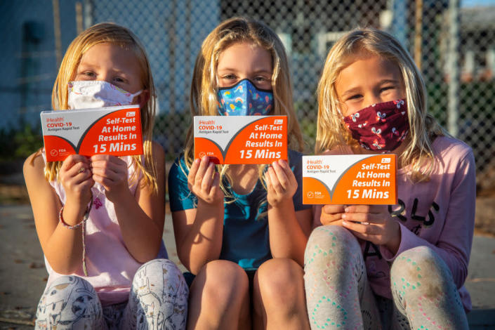 Kate Kahn, 5, Savannah Harper, 5 and Elyse Kahn, 7, from left, pose with their iHealth COVID-19 Antigen Rapid Tests, provided by the state of California, after receiving them at Tulita Elementary School, in Redondo Beach, on Thursday. (Jay L. Clendenin / Getty Images)