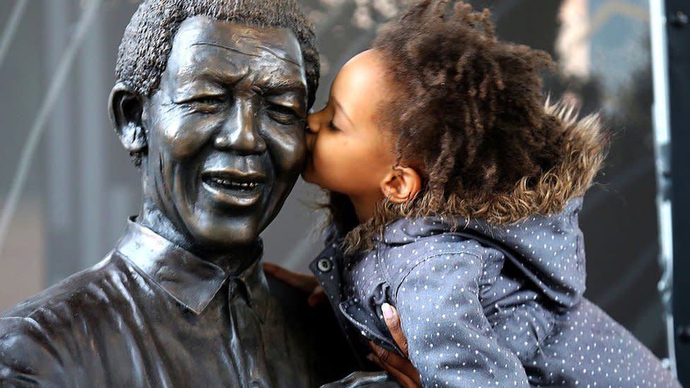A young South African girl names Malika is lifted by her mother to kiss a statue of former South African President Nelson Mandela before a service conducted by Archbishop Desmond Tutu at the Nelson Mandela Foundation on December 9, 2013 in Johannesburg, South Africa