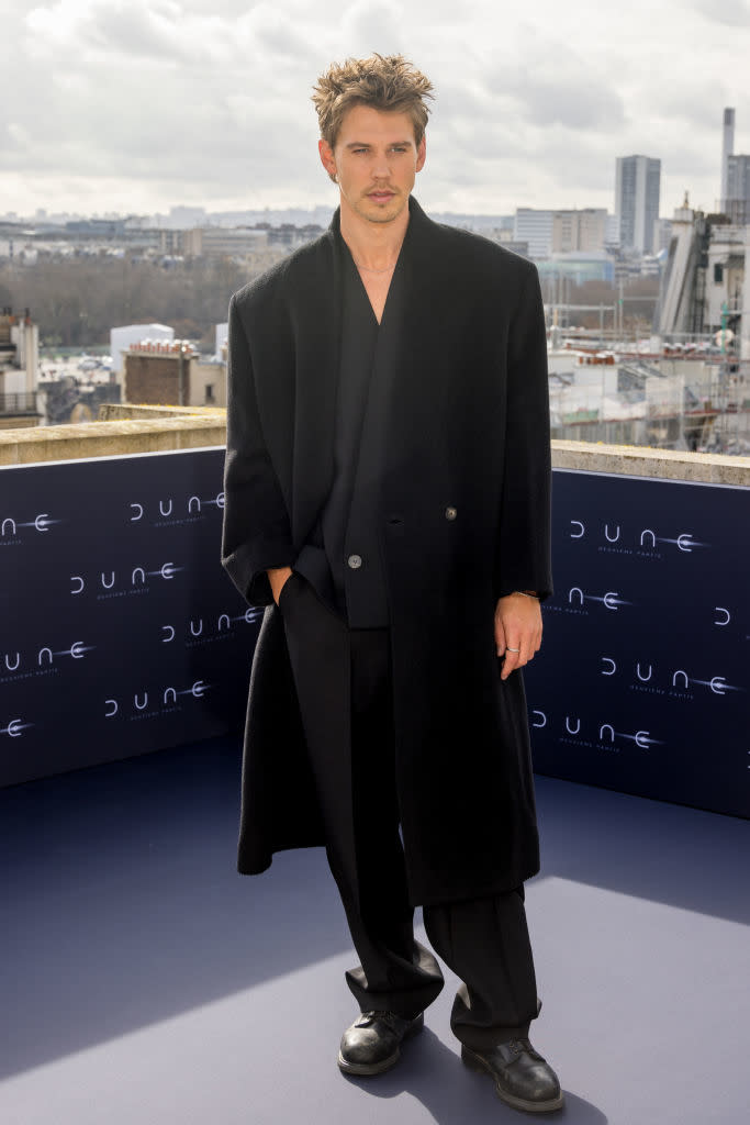 Austin in a stylish coat with cityscape backdrop, posing at a "Dune" event