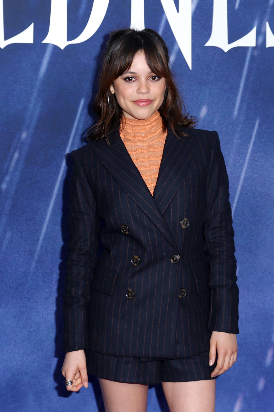 Jenna Ortega in a double-breasted blazer dress on a blue backdrop