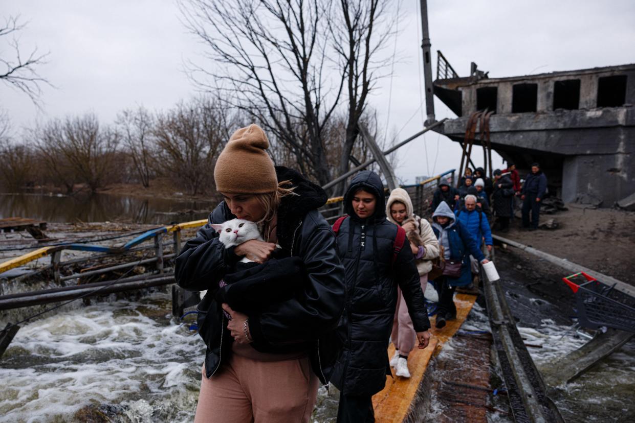 A woman holds her cat in her arms as evacuees cross a destroyed bridge.