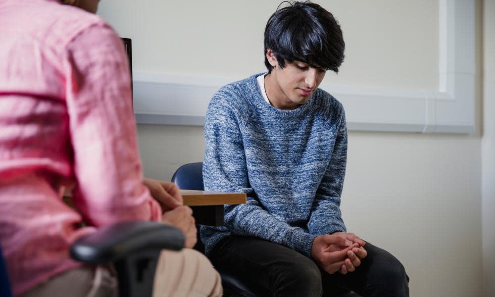 A female doctor talks to a young man who looks down