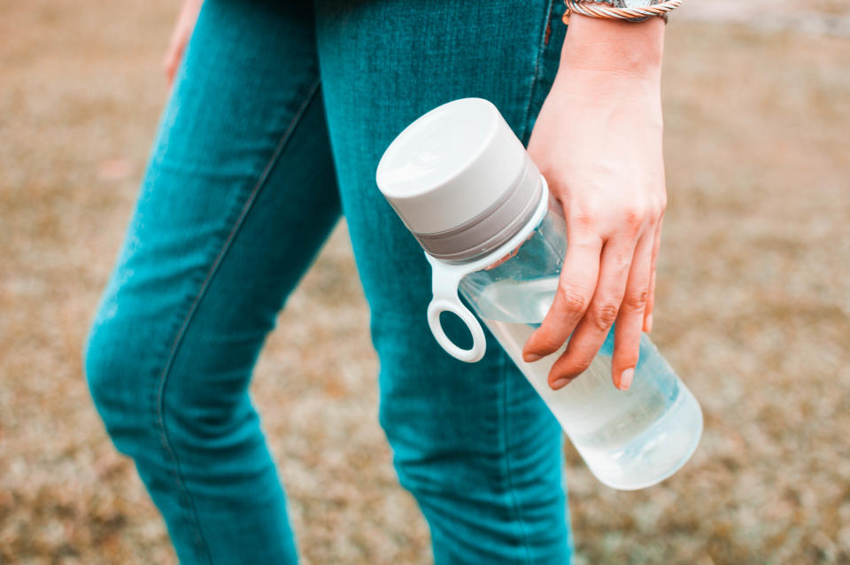 A close-up view of a young woman holding a reusable water bottle container outdoors