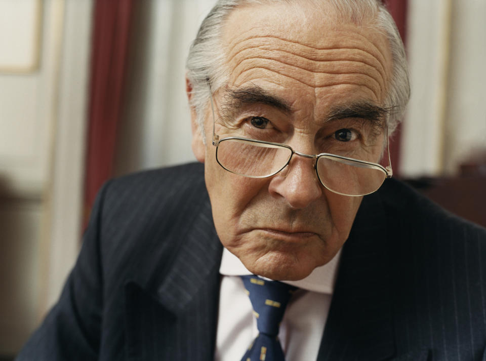 A visibly annoyed elderly man in a suit with a scowl on his face.