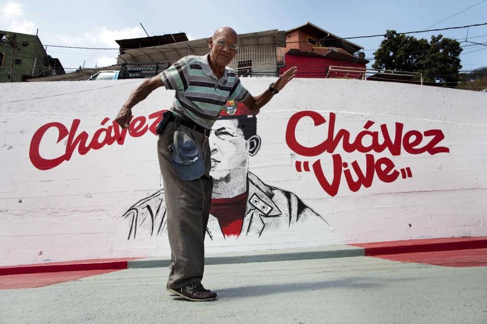 A man stops himself midstride after realizing he has walked into the framing of a picture, in front of a mural of Venezuela's late President Hugo Chavez in Caracas, Venezuela, Tuesday, March 4, 2014. He’s been dead a year, but Chavez’s face and voice are everywhere. He bangs out the national anthem on state radio every morning and the national guard has even blasted his voice reciting poetry to drive rock-throwing protesters off the street. To mark Chavez's passing, President Nicolas Maduro has decreed a 10-day-long commemoration - three days more than the weeklong official mourning period following his death at age 58 on March 5, 2013. (AP Photo/Rodrigo Abd)