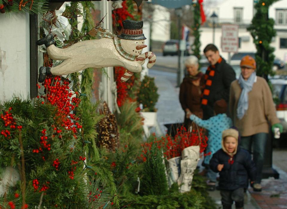 A family walks along a Hingham street decked out for the holidays as part of the Christmas in the Square festival.