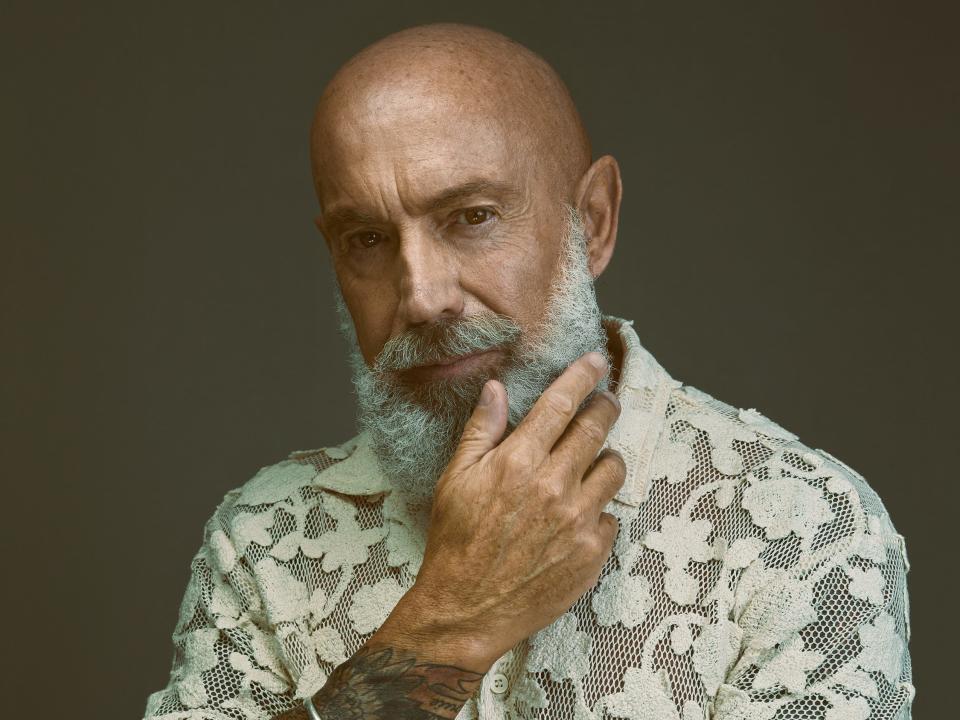 A mature male model with a gray beard wearing a patterned button-up shirt.