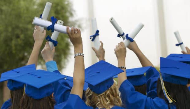 Group of Graduates Dressed in Graduation Gowns Holding Scrolls in the Air