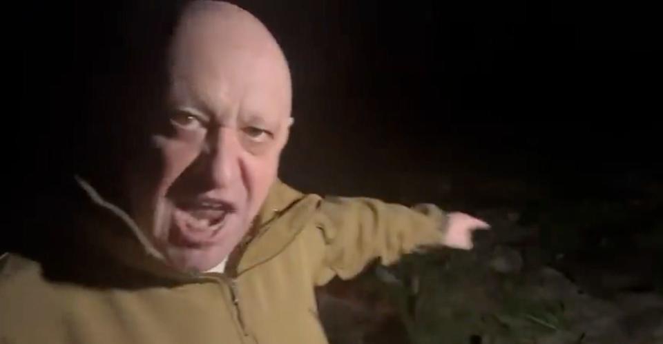 Yevgeny Prigozhin yells into the camera and points at rows of bodies behind him.