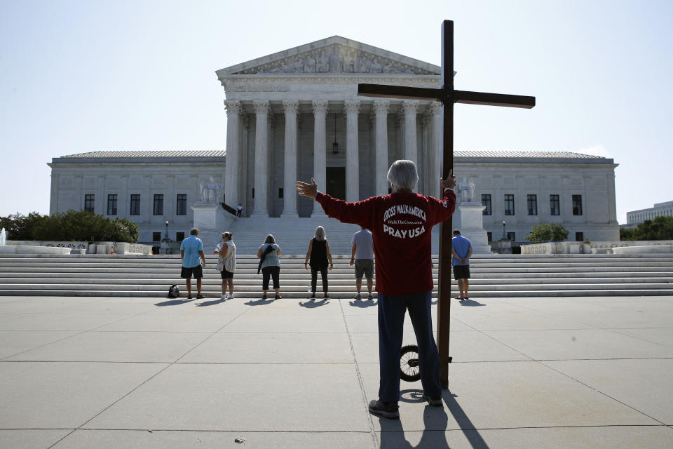 Tom Alexander holds a cross as he prays prior to rulings outside the Supreme Court on Capitol Hill in Washington, Wednesday, July 8, 2020. The Supreme Court is siding with two Catholic schools in a ruling that underscores that certain employees of religious schools, hospitals and social service centers can’t sue for employment discrimination.(AP Photo/Patrick Semansky)