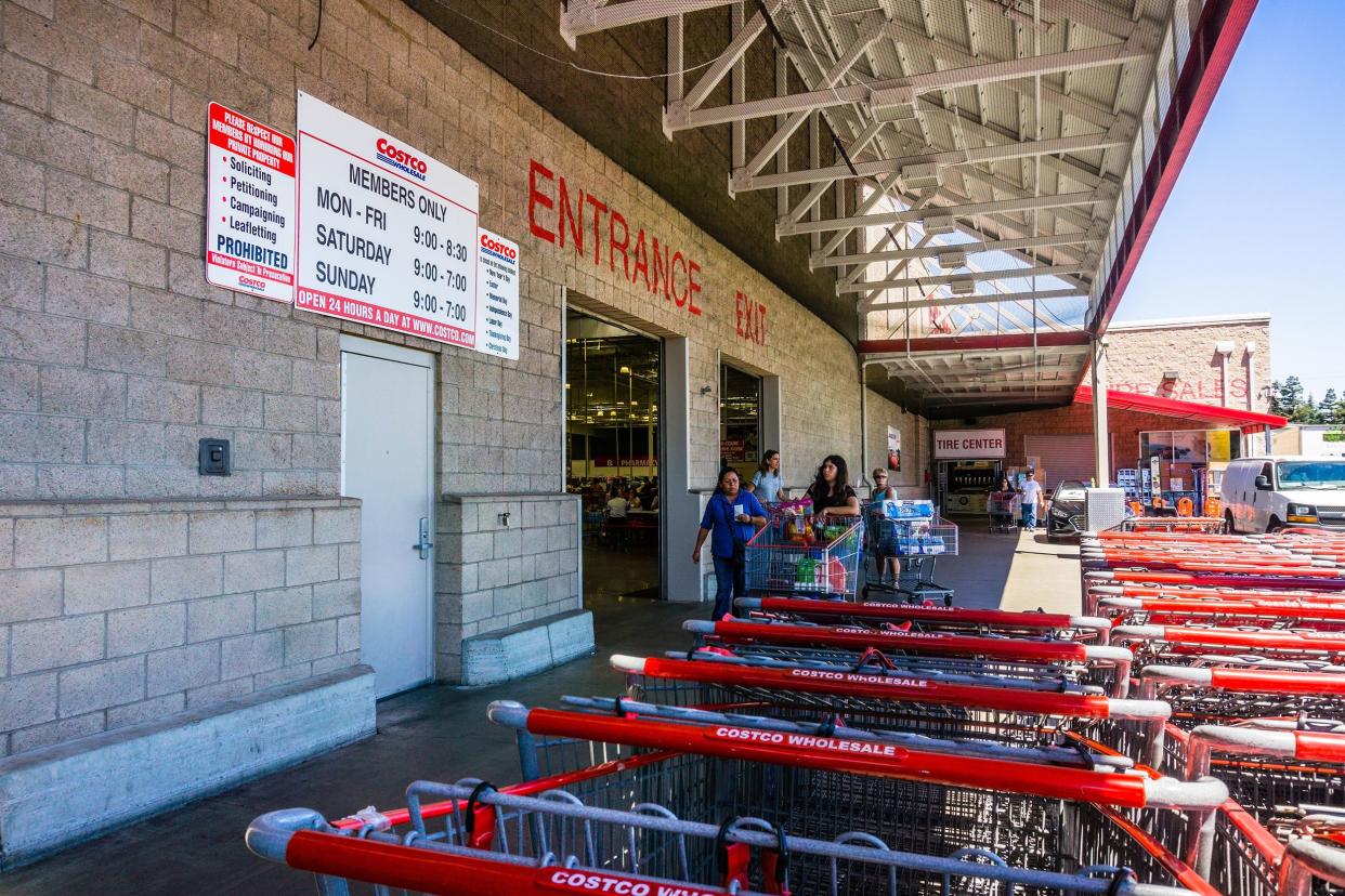 Entrance to Costco Wholesale in the South San Francisco Bay area, slight side-view, shopping carts in the foreground, people are entering, a bright sunny day, the parking lot is to the right