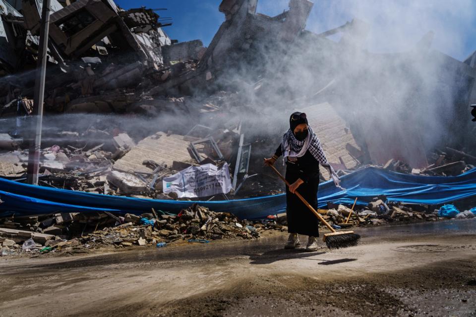 A Palestinian woman uses a broom next to a fallen building