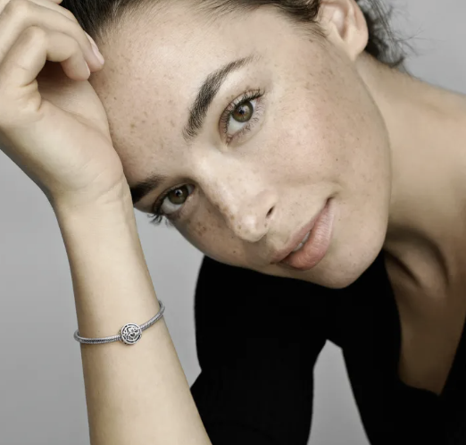 A young woman, wearing the Pandora Mum Hero Openwork Charm and bracelet looking into the camera