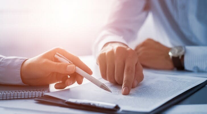 Image shows two people reviewing a written contract that sits on a desk between them. Asking the right questions and being clear about fees and services is important when hiring a financial advisor.