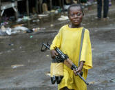 <p>A small boy brandishes an assault rifle near the front lines August 3, 2003 in Monrovia, Liberia. Very small children often hang around the fronts, learning to carry weapons in preparation as roles as fighters. Fighting has been dragging on for nearly two weeks now, leaving downtown’s social services nearly non-existent. (Photo by Chris Hondros/Getty Images) </p>