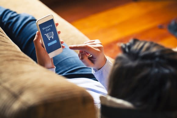 A person laying on a couch shopping from their smartphone.