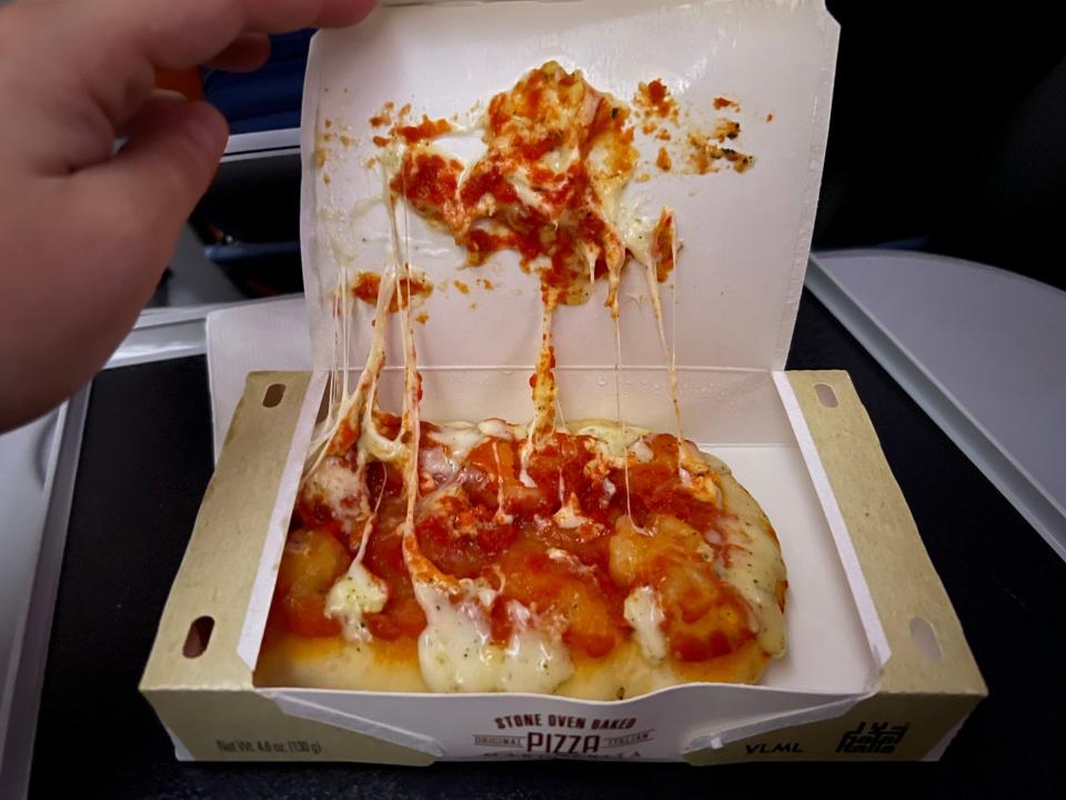 The pizza in its box with melted cheese.