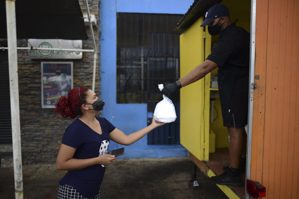 FILE - In this May 21, 2020 file photo, Yamirka Marmolejos, owner of a pet grooming business that has been closed since the start of the COVID-19 lockdown, takes a food order from Alfredo Gonzalez, both wearing masks as a precaution against the spread of the coronavirus, in Canovanas, Puerto Rico. More than 30,000 jobs have been lost because of the new coronavirus outbreak, and at least 1,400 businesses have closed. (AP Photo/Carlos Giusti, File)