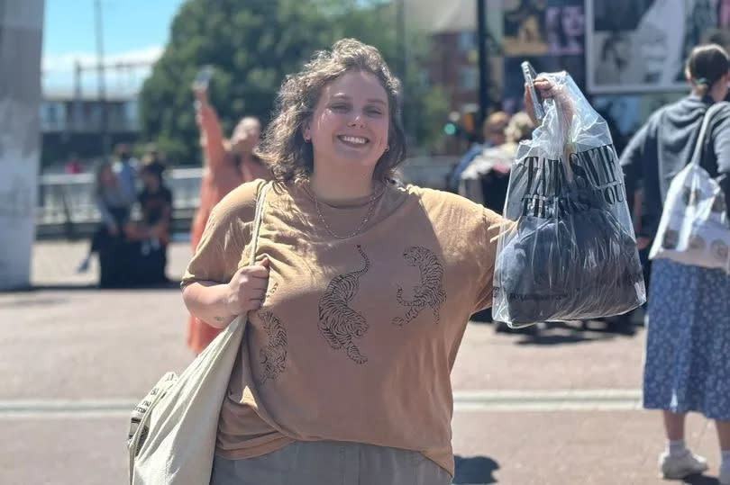 Woman smiling in sunshine the day before the Taylor Swift concert in Cardiff, with merchandise