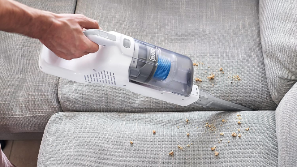 a hand using the stick vacuum in its handheld form to clean crumbs off a couch