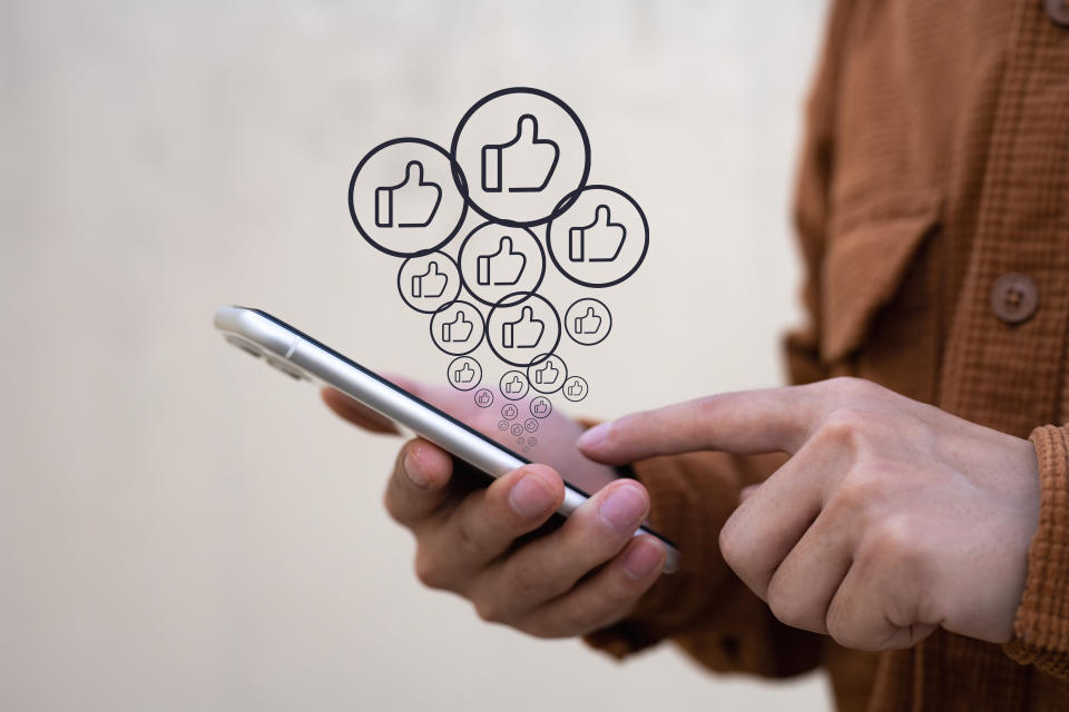 A man holds a smartphone and taps his finger on the screen showing many buttons for likes.