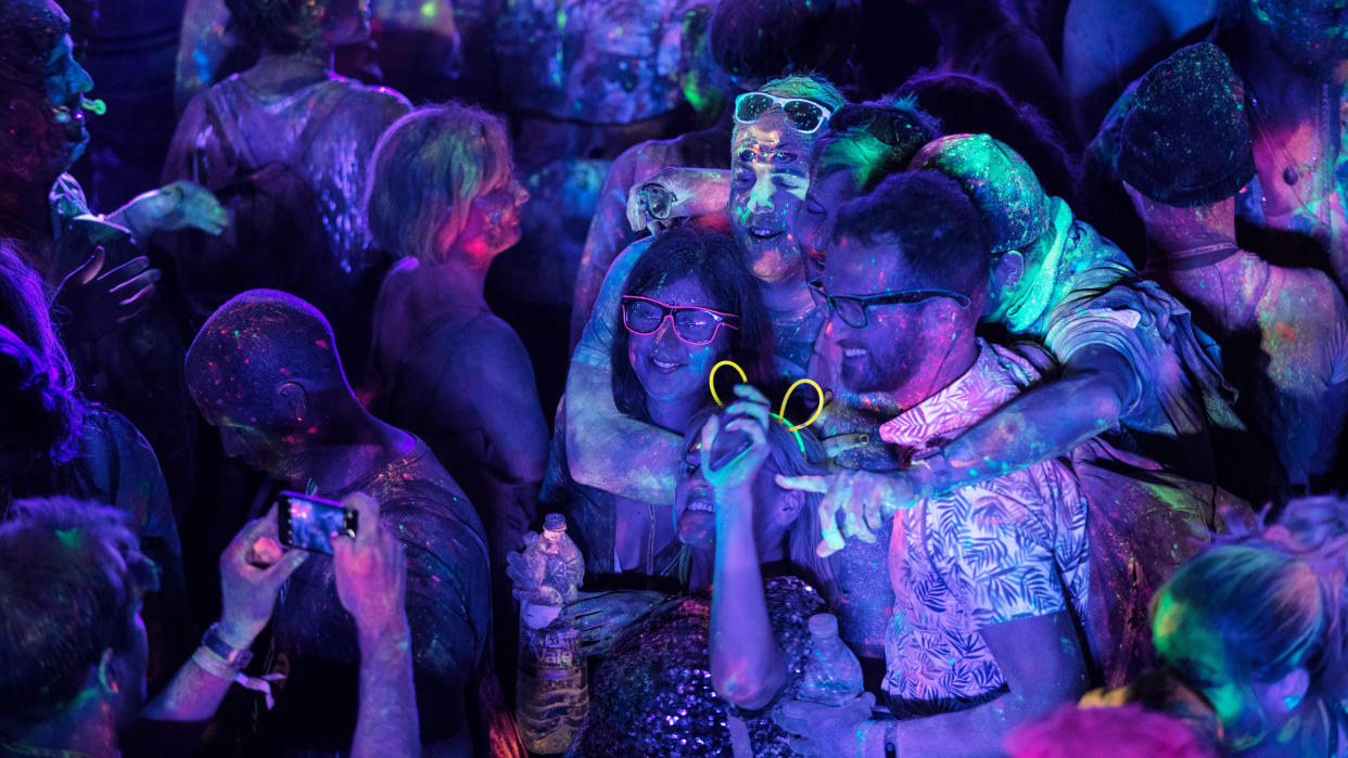  People at a party. There is a purple-tinted light and paint on the people is glowing under the UV light. 