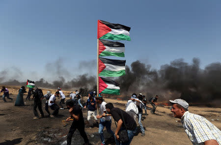 A demonstrator holds Palestinian flags as others run for cover during a protest marking al-Quds Day, (Jerusalem Day), at the Israel-Gaza border in the southern Gaza Strip June 8, 2018. REUTERS/Ibraheem Abu Mustafa