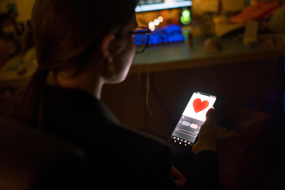 Person looking at a smartphone screen displaying a large red heart, indicating a romantic or dating app