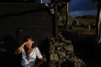 French-born artist Delphine Poulain shades her eyes, sitting outside her home as the sun sets in Hanga Roa, Rapa Nui, or Easter Island, Chile, Wednesday, Nov. 23, 2022. In addition to her artwork, Poulain has seven horses, earning some income by offering horseback riding for tourists. She sometimes sits outside her home, sipping wine, watching as her horses approach for their evening meal. (AP Photo/Esteban Felix)