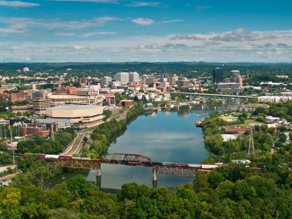 Aerial shot of Knoxville, Tennessee on a sunny and beautiful day in early Fall, looking down on the city from over the hills, along the Tennessee River past the University of Tennessee towards the downtown. A freight train is stopped on a bridge.