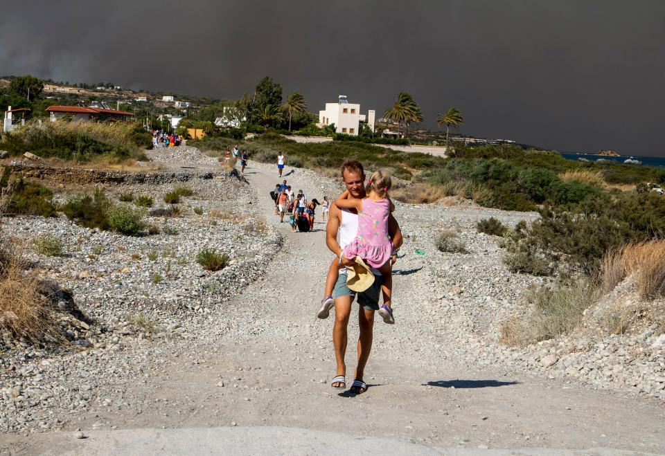 A man carries a child as they leave an area where a forest fire burns, on the island of Rhodes (AP)