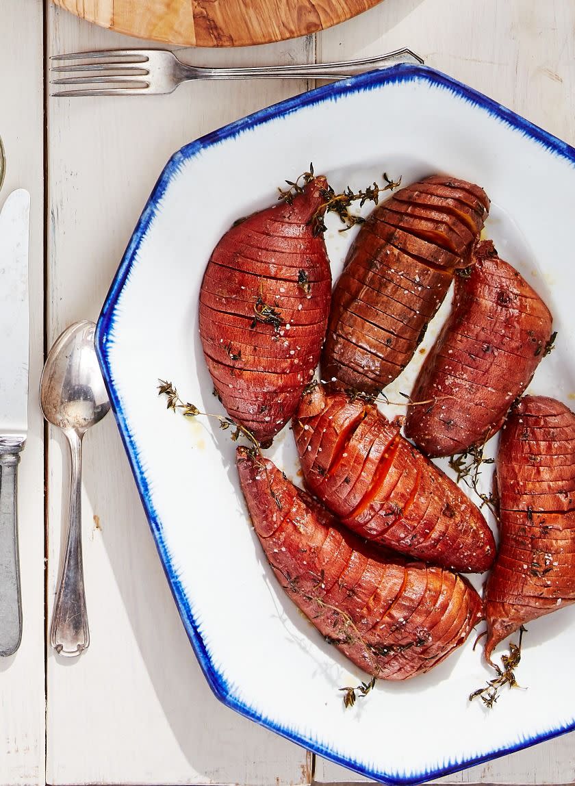 roasted hasselback sweet potatoes on a white serving plate with thyme and serving utensiles