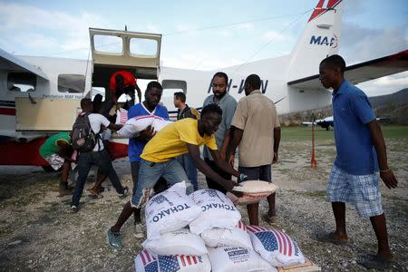 Men carry sacks of rice out from an airplane loaded with food at the airport in Jeremie. REUTERS/Carlos Garcia Rawlins