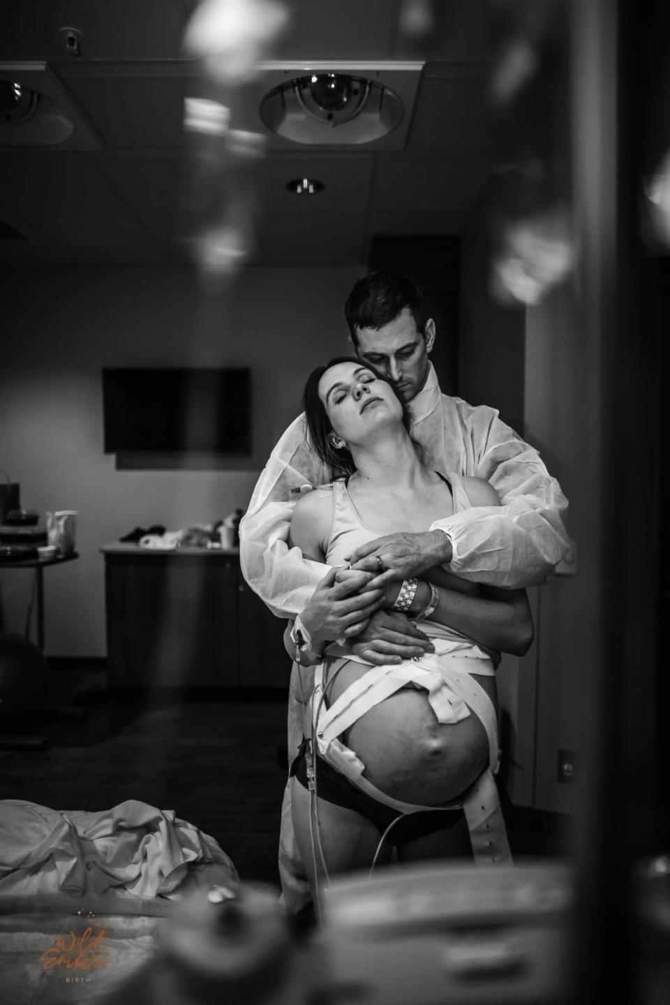 A standing pregnant woman in labor is embraced from behind by her husband