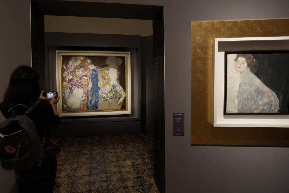 A woman admires Gustav Klimt's oil on canvas paintings "The Bride" (1918), left, and "Portrait of a Lady in White" (1917/18) on display at the exhibition "Klimt. The Secession and Italy" at the Museum of Rome, in Palazzo Braschi, Rome, during a press preview, Tuesday, Oct. 26, 2021. The exhibition, that explores Klimt's period in Italy, will be open to visitors from Oct.27, 2021 to March 27, 2022. (AP Photo/Andrew Medichini)