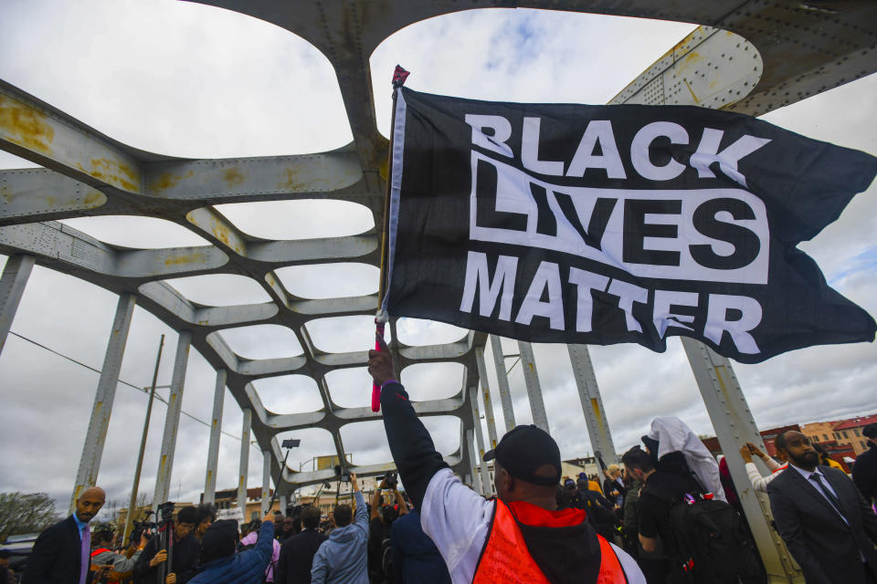 FILE - In this March 3, 2019, file photo, Black Lives Matter demonstrator waves a flag on the Edmund Pettus Bridge during the Bloody Sunday commemoration in Selma, Ala. Majorities of Americans across racial lines say white people are treated more fairly than black people by the police, according to a new poll from The Associated Press-NORC Center for Public Affairs Research. The dynamic has played out in the wake of the Black Lives Matter movement, which began in 2014 with the fatal shooting of unarmed 18-year-old Michael Brown by white, former Ferguson, Mo., police officer Darren Wilson. (AP Photo/Julie Bennett, File)
