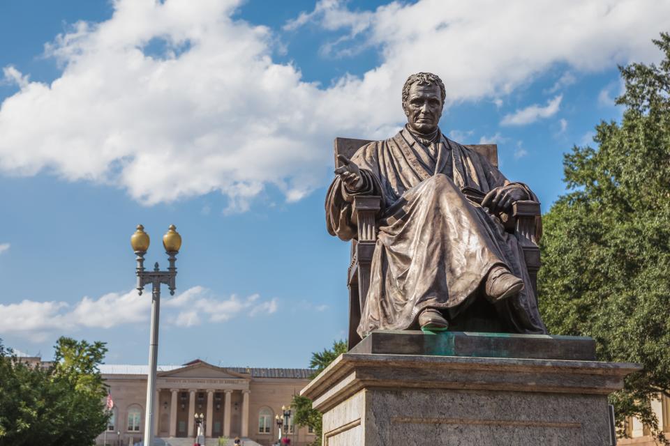 Bronze sculpture of John Marshall, fourth Chief Justice of the U.S. Supreme Court, located in John Marshall Park in Washington, D.C., with DC Court of Appeals in the background.
