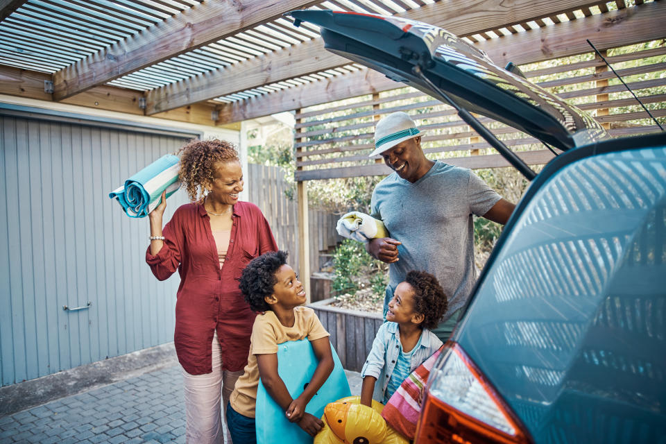 Carefree african american family unpacking the car at a holiday house. Happy mother and father smiling with their cute sons as they prepare the luggage to go on a road trip for summer vacation