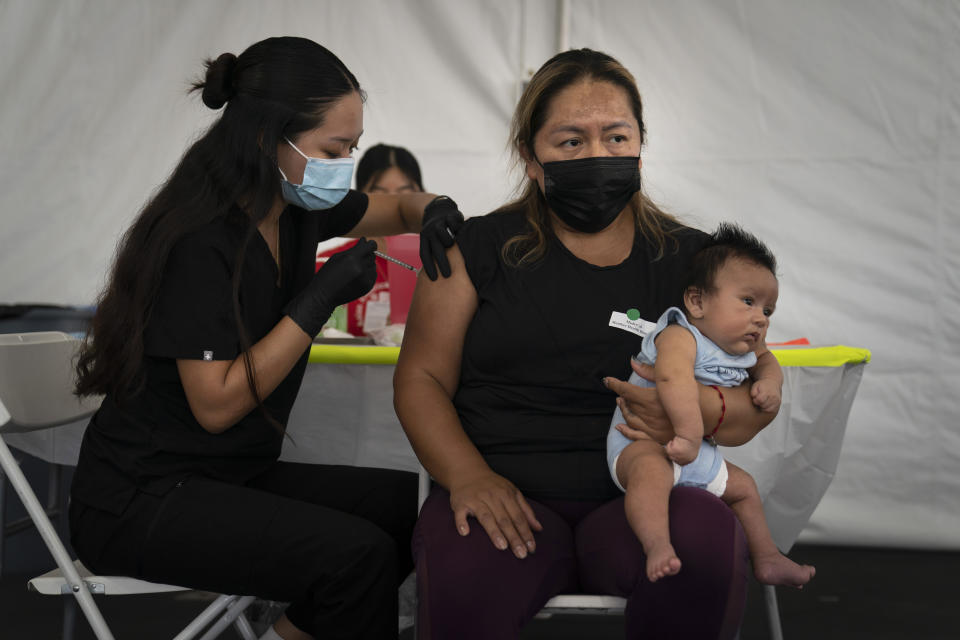 FILE - In this Aug. 28, 2021, file photo, Laura Sanchez, right, holds her 2-month-old son, Lizandro, while receiving the Pfizer COVID-19 vaccine from registered nurse, Noleen Nobleza at a vaccine clinic set up in the parking lot of CalOptima in Orange, Calif. COVID-19 deaths in the U.S. have climbed to an average of more than 1,900 a day for the first time since early March, with experts saying the virus is preying largely on a select group: 71 million unvaccinated Americans. (AP Photo/Jae C. Hong, File)