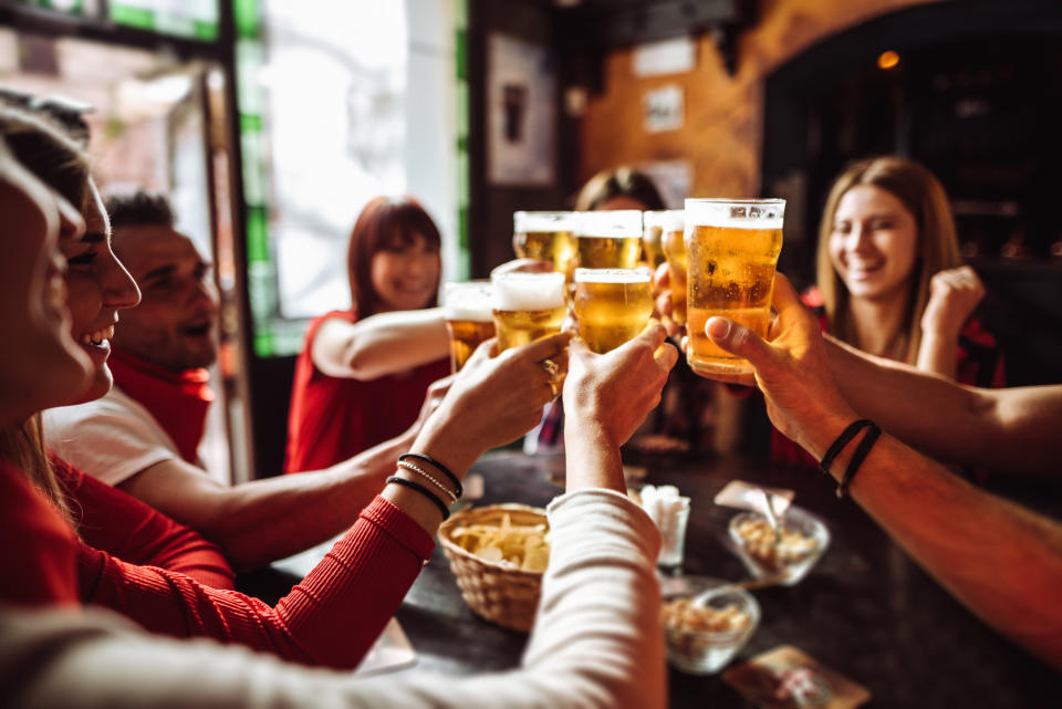 People cheers with their beers inside a pub. 