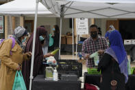 A sign for a King County (Wash.) Public Health COVID-19 vaccination clinic located at the Tukwila Village Farmers Market — which features produce grown locally by members of immigrant and refugee communities — is shown as people shop, Wednesday, Sept. 22, 2021, in Tukwila, Wash., south of Seattle. The clinic will be at the market weekly through at least most of October. (AP Photo/Ted S. Warren)