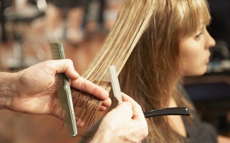 Male hairdresser cutting young woman's hair with razor