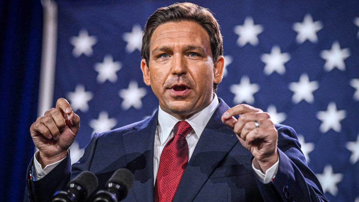 Ron DeSantis speaks into microphones in front of an American flag.