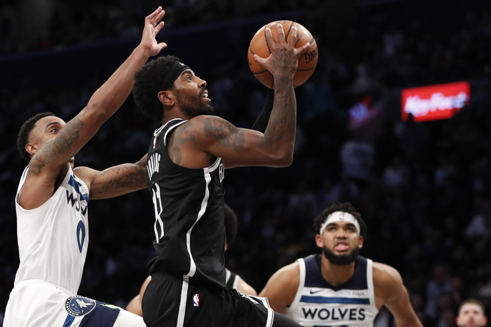 Minnesota Timberwolves guard Jeff Teague (0) defends against Brooklyn Nets guard Kyrie Irving (11) as Irving goes up for a shot in overtime of an NBA basketball game Wednesday, Oct. 23, 2019, in New York. Timberwolves' Karl Anthony-Towns is at right. Irving had 50 points but the Timberwolves won 127-126. (AP Photo/Kathy Willens)