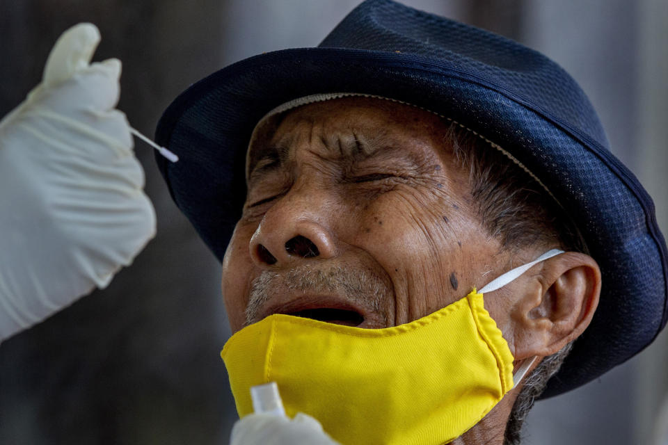 A man grimaces as a nasal swab sample is collected from him to test for a new coronavirus in Bangkok, Thailand, Wednesday, May 6, 2020. Thai health workers started testing community of about 1,600 people of Klong Toey slum at a nearby Buddhist temple. (AP Photo/Gemunu Amarasinghe)