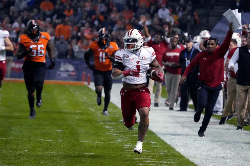 Wisconsin running back Chez Mellusi (1) runs away from Oklahoma State defensive tackle Xavier Ross (56) and linebacker Lamont Bishop during the first half of the Guaranteed Rate Bowl NCAA college football game Tuesday, Dec. 27, 2022, in Phoenix. (AP Photo/Rick Scuteri)