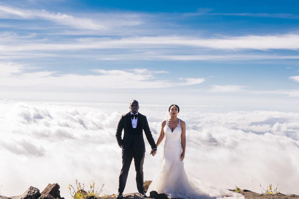 A bride and groom hold hands in front of clouds.