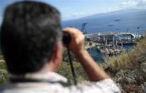 A person looks on with binoculars as the capsized cruise liner Costa Concordia lies on its side next to Giglio Island September 16, 2013. REUTERS/Tony Gentile