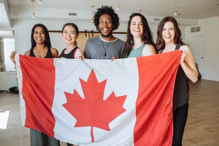 Five smiling people hold a Canadian flag indoors